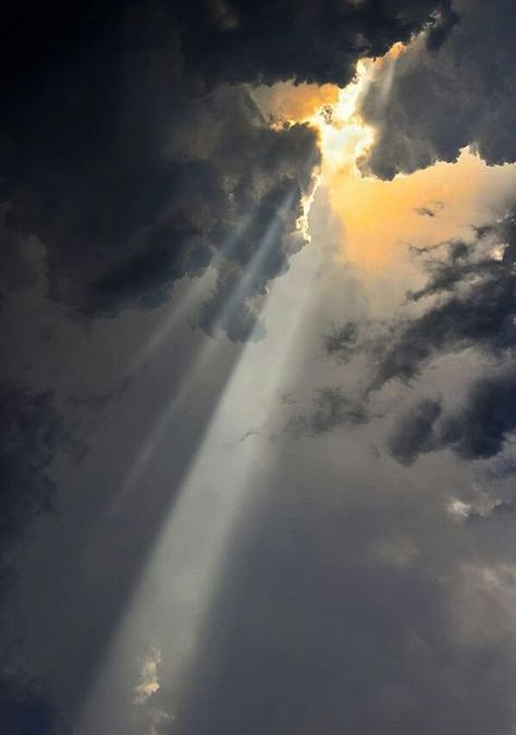 Rays of sunlight breaking through dark clouds, illuminating a small section of the sky with a warm, golden glow.