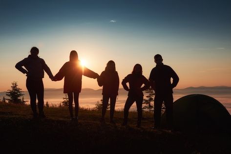 A group of individuals gathered in front of a tent, silhouetted against a vibrant sunset backdrop.